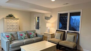 Un salon avec un canapé bleu clair, une table basse blanche, un canapé beige, un meuble en bois et une fenêtre donnant sur un balcon.
