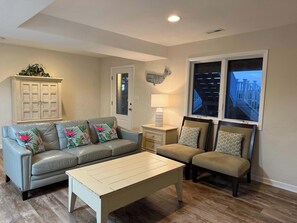 A living room with a light blue sofa, a white coffee table, a beige sofa, a wooden cabinet, and a window with a view of a balcony. - Sunlit 3-story home with private in-ground pool, balcony, washer/dryer (Virginia Beach)