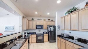 A modern kitchen with wooden cabinets, a black refrigerator, a microwave, and a stove. - Second-floor, ocean view condo with balcony, foosball, WiFi & on-site pool/gym (Virginia Beach)