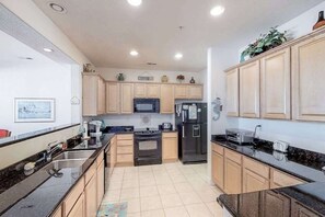 A modern kitchen with wooden cabinets, a black refrigerator, a microwave, and a stove. - Second-floor, ocean view condo with balcony, foosball, WiFi & on-site pool/gym (Virginia Beach)