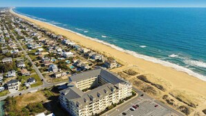 An aerial view of a coastal residential area with a large hotel building, a beach, and a clear blue sky. - Second-floor, ocean view condo with balcony, foosball, WiFi & on-site pool/gym (Virginia Beach)