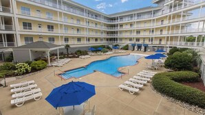 A multi-story hotel with a central swimming pool, outdoor seating, and a landscaped garden. - Second-floor, ocean view condo with balcony, foosball, WiFi & on-site pool/gym (Virginia Beach)