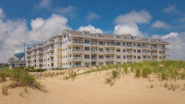 A multi-story hotel with balconies, located on a sandy beach with dunes. - Second-floor, ocean view condo with balcony, foosball, WiFi & on-site pool/gym (Virginia Beach)