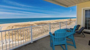 A balcony with a view of the beach, a table, and two chairs. - Oceanfront, corner condo with wrap-around deck, great views & on-site pool/gym (Virginia Beach)
