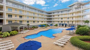 A multi-story hotel with a central swimming pool, outdoor seating, and a well-maintained garden. - Oceanfront, corner condo with wrap-around deck, great views & on-site pool/gym (Virginia Beach)
