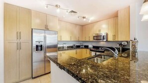 A modern kitchen with stainless steel appliances, granite countertops, and light wood cabinetry. - Beach condo with pool views, balcony, outdoor pool & gym (Virginia Beach)