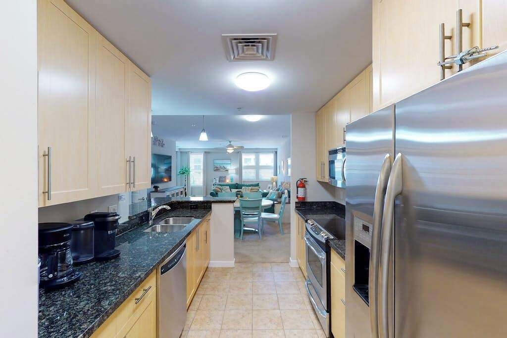 A modern kitchen with stainless steel appliances, a dining area with a table and chairs, and a visible ceiling vent.
