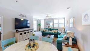 Een woonkamer met een televisie, een smaragdgroene bank en een eethoek met een ronde tafel.