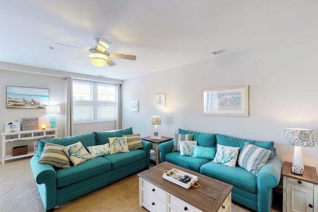 Ein Wohnzimmer mit türkisfarbenen Sofas, einem Holztisch und einem Deckenventilator.