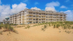 Hotel com vários andares e varandas, situado numa praia arenosa com céu claro.
