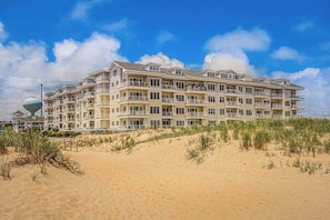 Ein mehrstöckiges Hotel mit Balkonen, direkt an einem Sandstrand unter blauem Himmel gelegen.