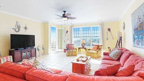 Uma sala de estar com um sofá vermelho grande, uma televisão e um ventilador de teto.