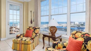 Quarto com vista para a praia, um sofá, uma mesa com abajur e uma guitarra na parede.