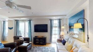 Ein Wohnzimmer mit Deckenventilator, Flachbildfernseher, Sofa, Couchtisch und einem Gemälde mit Strandmotiv.