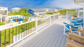 Une terrasse avec une piscine, des chaises longues et une vue sur les maisons et l’océan.