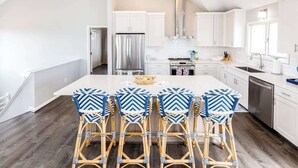 Une cuisine moderne avec des meubles blancs, un îlot central et quatre tabourets de bar aux motifs bleus et blancs.