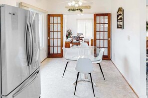 A kitchen with a stainless steel refrigerator, a dining table with chairs, and a wooden door with glass panels. - Tranquil home steps from the water w/private pool, WiFi, private washer/dryer (Virginia Beach)