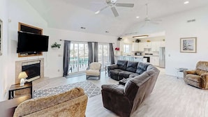 A spacious living room with a flat-screen TV, a fireplace, a sofa, and a dining area with a kitchen in the background. - Tranquil home steps from the water w/private pool, WiFi, private washer/dryer (Virginia Beach)