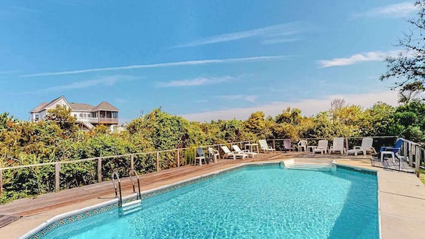 A swimming pool with lounge chairs and a wooden deck, surrounded by greenery and a house in the background. - Tranquil home steps from the water w/private pool, WiFi, private washer/dryer (Virginia Beach)