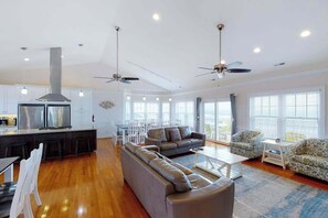 A spacious living area with a sofa, coffee table, and chairs, a kitchen with a central island, and a ceiling fan. - Oceanfront home with elevator, pool, game room, private washer/dryer, & WiFi (Virginia Beach)