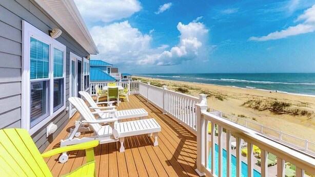 Eine Holzterrasse mit weißen Geländern, einem Pool und Blick auf den Strand.