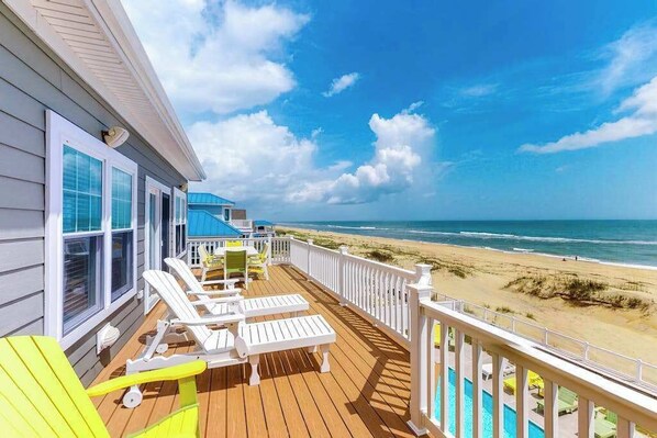 A wooden deck with white railings, a pool, and a view of the beach. - Oceanfront home with elevator, pool, game room, private washer/dryer, & WiFi (Virginia Beach)