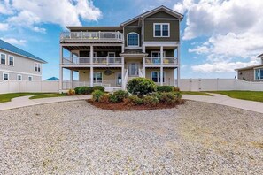 A two-story building with a balcony, a front porch, and a gravel driveway. - Oceanfront home with elevator, pool, game room, private washer/dryer, & WiFi (Virginia Beach)