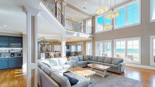 A spacious living area with a large sectional sofa, a coffee table, and a view of the ocean through large windows. - Wonderful beachfront home w/private indoor & outdoor pools, WiFi, AC, deck (Virginia Beach)