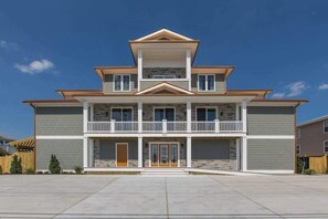 A two-story building with a balcony on the second floor, a front entrance with glass doors, and a clear sky. - Wonderful beachfront home w/private indoor & outdoor pools, WiFi, AC, deck (Virginia Beach)