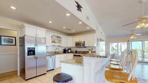 A modern kitchen with white cabinets, stainless steel appliances, a granite countertop, and a bar area with wooden chairs. - 8 BDR & 7.5 BA Luxury Beach House w/private pool & hot tub (Virginia Beach)