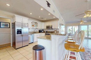 A modern kitchen with white cabinets, stainless steel appliances, a granite countertop, and a bar area with wooden chairs. - 8 BDR & 7.5 BA Luxury Beach House w/private pool & hot tub (Virginia Beach)