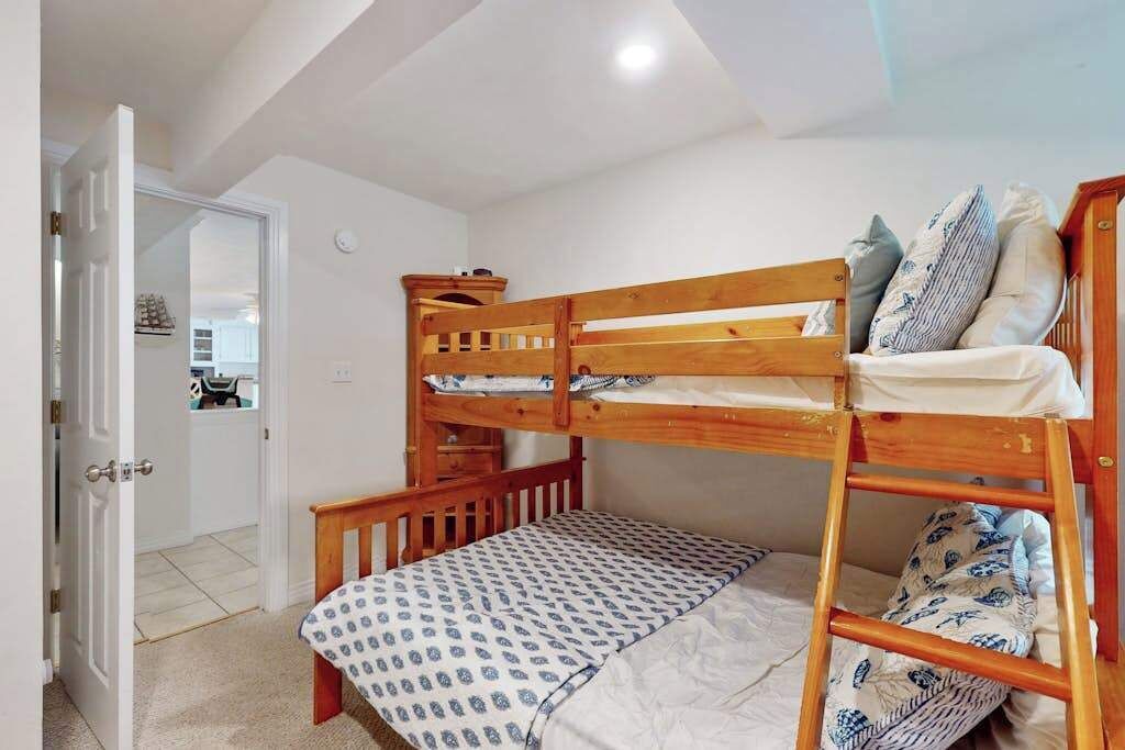 Un llit superposat amb estructura de fusta, un llençol estampat i almoines. Una porta condueix a una altra habitació.