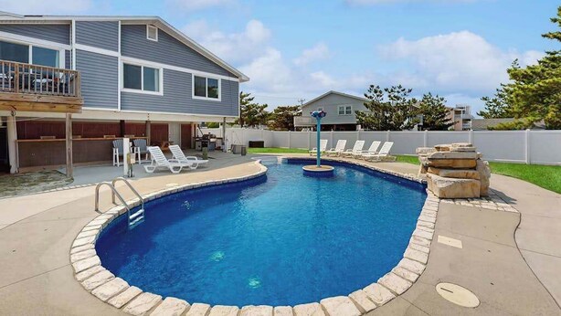 Une piscine résidentielle bordée de pierres, dotée d’une terrasse en bois et d’un espace patio couvert.