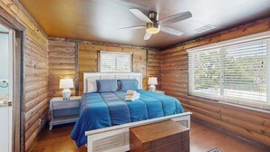 Une chambre à coucher avec un lit, des tables de chevet, un ventilateur de plafond et de grandes fenêtres.