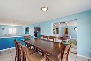 A spacious dining area with a long wooden table and chairs, a kitchen in the background, and a living area with a sofa and a ceiling fan. - Dog-friendly home near the beach w/private W/D, WiFi, private H/T & pool, AC (Virginia Beach)