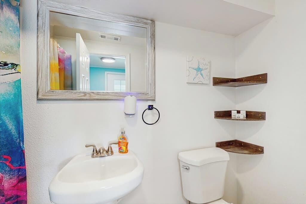 A bathroom with a white sink, a toilet, a mirror, and wooden shelves.