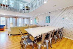 A spacious living area with a dining table and chairs, a sofa, and a staircase leading to an upper level. - Dog-Friendly, Ocean View Beach Retreat w/Private Outdoor Pool, Decks & A/C (Virginia Beach)