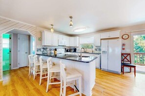 A modern kitchen with white cabinets, a central island with bar stools, a built-in oven, and a refrigerator. - Dog-Friendly, Ocean View Beach Retreat w/Private Outdoor Pool, Decks & A/C (Virginia Beach)