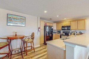 A kitchen with wooden cabinets, a refrigerator, a microwave, and a sink. - Sunny Condo w/Shared Outdoor Pool, Central A/C, Private W/D - Near the Ocean (Virginia Beach)