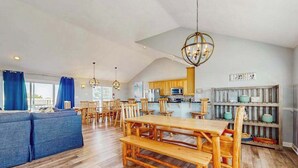 Amplia sala de estar con mesa de comedor de madera, sofá azul y una cocina al fondo.
