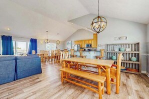 A spacious living area with a wooden dining table, blue sofa, and a kitchen in the background. - Dog-friendly home with pool, hot tub, lazy river, splash pad, & game room (Virginia Beach)