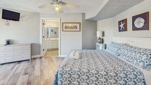 Un dormitorio con cama, ventilador de techo, televisión y puerta que da a un baño.