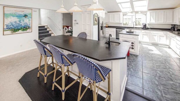 Una cocina moderna con una isla central, taburetes de bar, iluminación colgante y una escalera que sube a otro nivel.