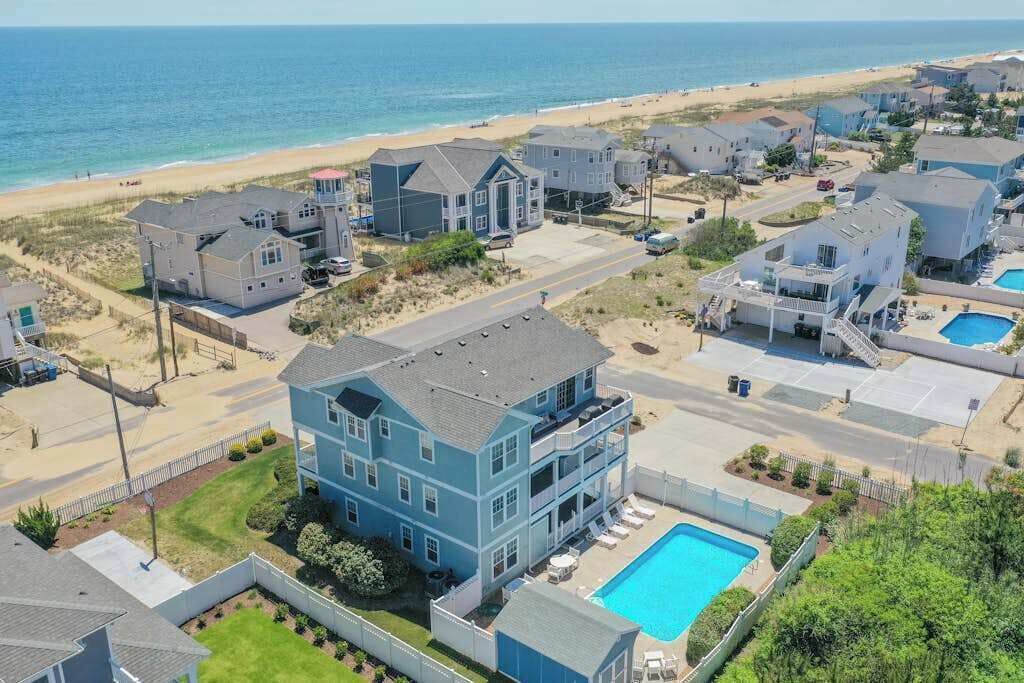 A coastal residential area with houses, a swimming pool, and a beach in the background.