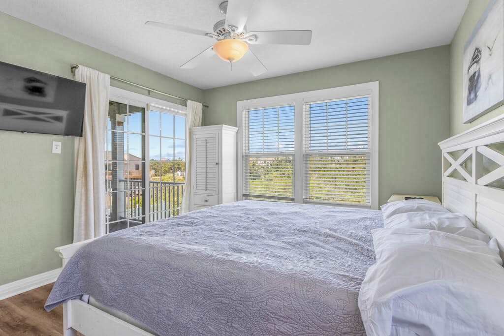A bedroom with a bed, a ceiling fan, a TV mounted on the wall, and a balcony with a view.