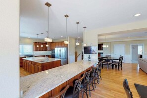 A modern kitchen with a large island, bar stools, wooden cabinets, and pendant lighting. - Oceanfront home w/elevator, private outdoor pool & hot tub - wedding-friendly (Virginia Beach)