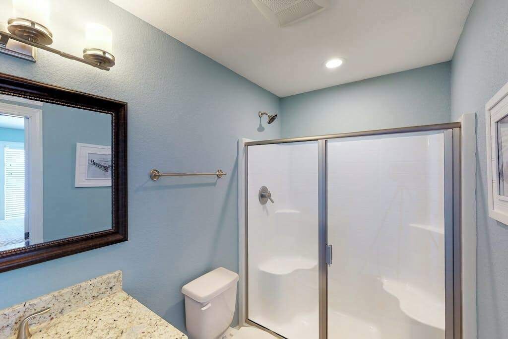 A bathroom with a shower, toilet, sink, and a mirror.