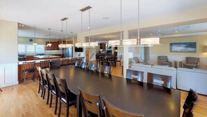 Un comedor amplio con una mesa larga y sillas, una cocina equipada con electrodomésticos modernos, y una sala de estar con sofá y sillas.