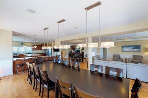 A spacious dining area with a long table and chairs, a kitchen area with modern appliances, and a living area with a sofa and chairs. - Oceanfront home w/elevator, private outdoor pool & hot tub - wedding-friendly (Virginia Beach)