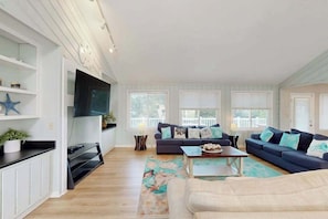 A living room with a dark blue sofa set, a flat-screen TV mounted on the wall, and a wooden coffee table. - Fantastic home with private pool, hot tub, Ping-Pong, billiards & fast WiFi (Virginia Beach)